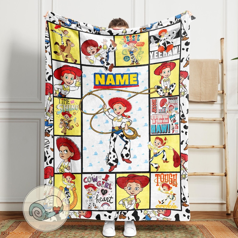 Op de afbeelding: Een wit en zwart deken met illustraties van Jessie uit Toy Story. De deken heeft een koeienprint rand en een centraal paneel met het woord "NAME". Jessie wordt afgebeeld met een lasso.