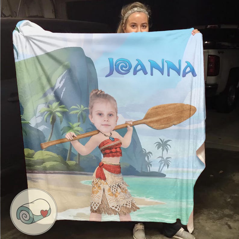 May include: A personalized blanket featuring a cartoon illustration of a young girl in a Polynesian outfit, holding a wooden oar. The blanket has a beach scene background with the name "Joanna" in blue script. The blanket is light blue and white.