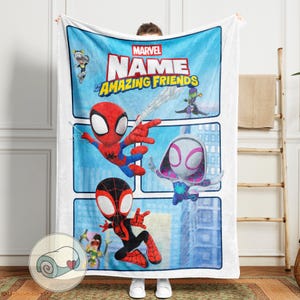May include: A white blanket featuring the Marvel logo and the words "NAME and his Amazing Friends." The blanket showcases cartoon illustrations of Spider-Man, Spider-Gwen, and Miles Morales in action poses against a blue sky backdrop.