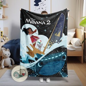 May include: Black Moana 2 blanket featuring a vibrant illustration of Moana, Pua, and Hei Hei sailing on a boat. The design includes a dark blue whale, waves, and stars. The blanket is a cozy home decor item.