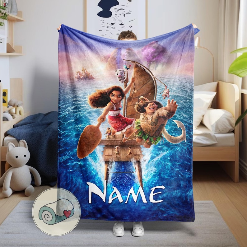 Może przedstawiać: Niebieski koc z żywą ilustracją postaci z popularnego filmu animowanego. Projekt zawiera ł&oacute;dź, fale oceanu i słowo "NAME" w kolorze białym. Koc jest trzymany przez osobę.