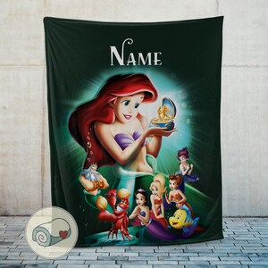 May include: A dark green blanket featuring a colorful illustration of Ariel from The Little Mermaid. Ariel is holding a treasure box, surrounded by other characters from the movie. The word "Name" is at the top.