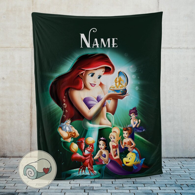 May include: A dark green blanket featuring a colorful illustration of Ariel from The Little Mermaid. Ariel is holding a treasure box, surrounded by other characters from the movie. The word "Name" is at the top.