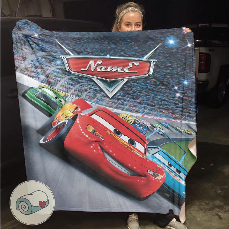 May include: A plush blanket featuring Lightning McQueen from the animated movie Cars. The blanket has a vibrant design with a race track background and the word "Name" in a stylized font. The blanket is primarily red, blue, and green.