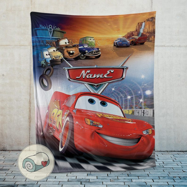 May include: A plush blanket featuring characters from the animated movie Cars. The blanket showcases Lightning McQueen racing on a track, with other characters and the movie's logo. The background includes a scenic desert landscape.