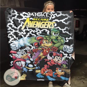 Puede incluir: Una manta negra con una ilustraci&oacute;n de estilo c&oacute;mic de personajes de Disney como Vengadores. La manta tiene el texto "Mickey and Friends Became The Avengers" en amarillo y blanco. El fondo tiene un patr&oacute;n blanco y negro.
