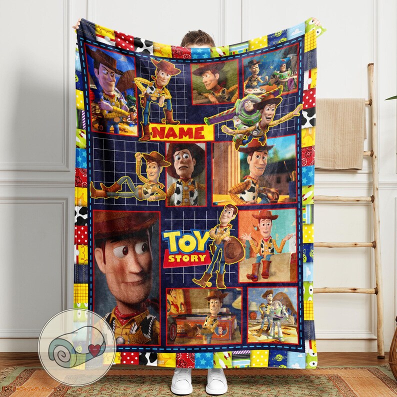 May include: A plush, rectangular blanket featuring a collage of images from the animated film "Toy Story." The design includes various character portraits and the film's logo. The blanket has a patchwork border with a blue grid background and the word "NAME" in yellow.
