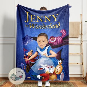 May include: A blue fleece blanket featuring a custom illustration of a person as Alice in Wonderland. The blanket has the text "JENNY in Wonderland" in gold lettering. The design includes the Cheshire Cat, the White Rabbit, and the Queen of Hearts.