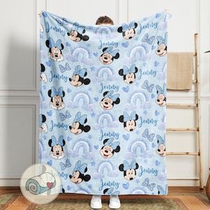 Puede incluir: Una manta azul claro con un estampado repetido de Minnie Mouse, lazos, arco&iacute;ris y corazones. El nombre "Jenny" est&aacute; escrito en el dise&ntilde;o. Esta suave manta es ideal para un dormitorio infantil o como regalo.