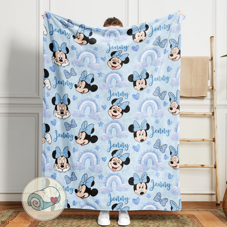 Puede incluir: Una manta azul claro con un estampado repetido de Minnie Mouse, lazos, arco&iacute;ris y corazones. El nombre "Jenny" est&aacute; escrito en el dise&ntilde;o. Esta suave manta es ideal para un dormitorio infantil o como regalo.