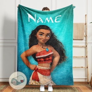 K&ouml;nnte beinhalten: Eine t&uuml;rkisfarbene Decke mit einer Cartoon-Illustration einer Frau mit langen schwarzen Haaren, die ein rotes Oberteil und einen wei&szlig;en Rock tr&auml;gt. Das Wort "NAME" ist oben in Wei&szlig; aufgedruckt. Eine aufgerollte Decke mit einem Herzen befindet sich in der Ecke.