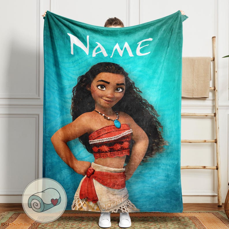 K&ouml;nnte beinhalten: Eine t&uuml;rkisfarbene Decke mit einer Cartoon-Illustration einer Frau mit langen schwarzen Haaren, die ein rotes Oberteil und einen wei&szlig;en Rock tr&auml;gt. Das Wort "NAME" ist oben in Wei&szlig; aufgedruckt. Eine aufgerollte Decke mit einem Herzen befindet sich in der Ecke.