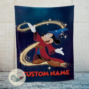 Op de afbeelding: Een marineblauwe deken met een cartoonafbeelding van Mickey Mouse als tovenaar, gekleed in een rode mantel en blauwe hoed. Het ontwerp bevat gouden wervelingen en de tekst "CUSTOM NAME" in het rood. De deken wordt tegen een neutrale achtergrond getoond.