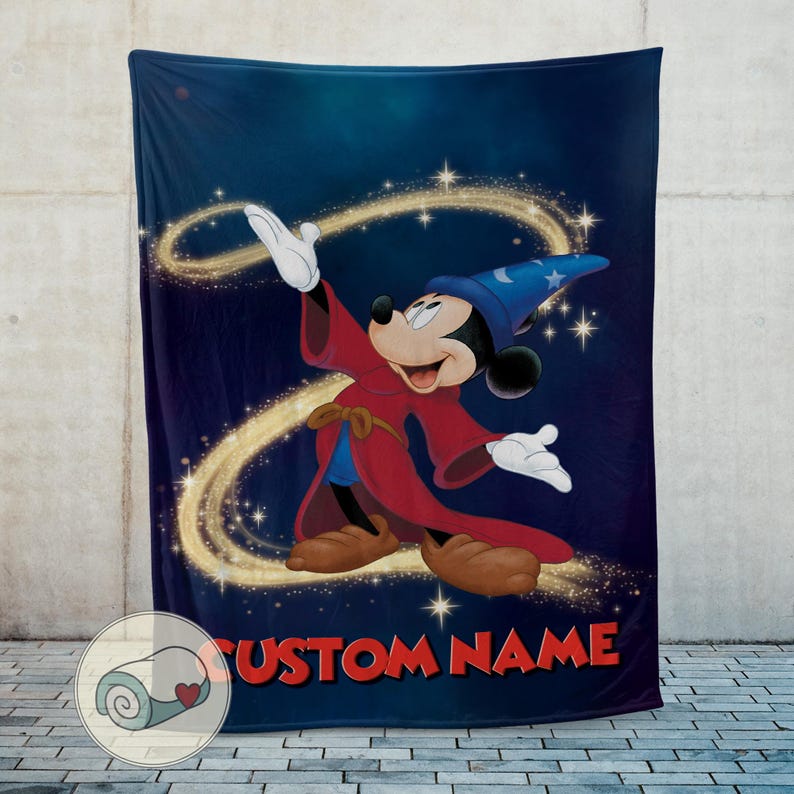 Op de afbeelding: Een marineblauwe deken met een cartoonafbeelding van Mickey Mouse als tovenaar, gekleed in een rode mantel en blauwe hoed. Het ontwerp bevat gouden wervelingen en de tekst "CUSTOM NAME" in het rood. De deken wordt tegen een neutrale achtergrond getoond.