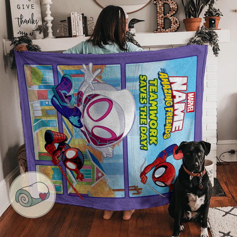 Op de afbeelding: Een rechthoekige Marvel-deken met Spider-Man en Spider-Gwen. De deken heeft een paarse rand en een blauwe achtergrond met de woorden "Amazing Friends" en "Teamwork Saves the Day!" erop gedrukt.