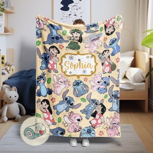 Pu&ograve; includere: Una coperta beige con un motivo ripetuto di personaggi dei cartoni animati in varie pose. La coperta ha una cornice color oro con il nome "Sophia" al centro. I personaggi sono in tonalit&agrave; di blu, rosa e rosso.