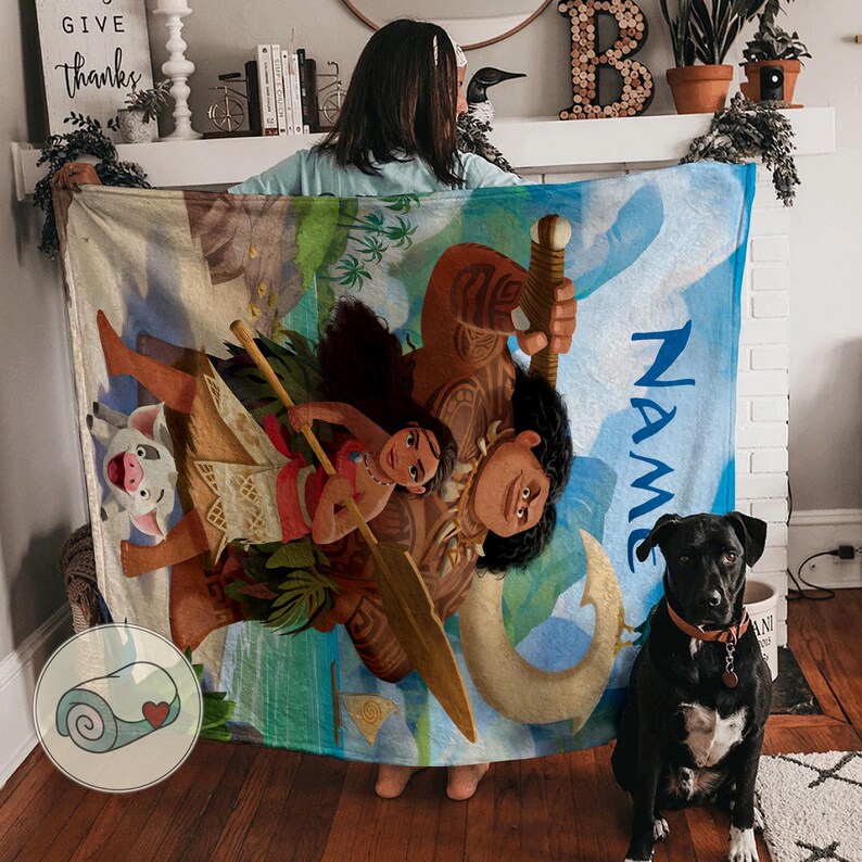 May include: A large, rectangular blanket featuring a colorful illustration of characters from a popular animated movie. The blanket has a blue background with the word "NAME" printed on it. A black dog sits in front of the blanket.