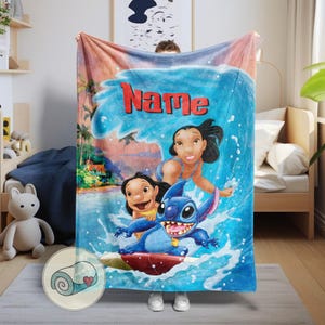 May include: A blue blanket featuring a cartoon scene with the word "Name" in red. The design includes characters, a blue wave, and a tropical background. The blanket is held up by a person.
