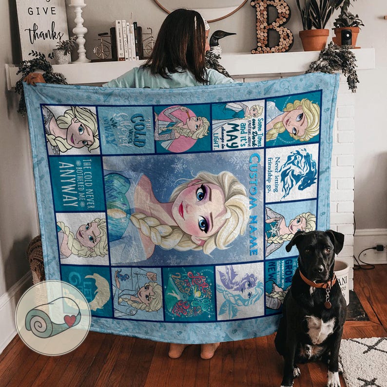 May include: A light blue blanket featuring Elsa from Frozen, with various images and quotes. The blanket has a light blue border and includes the text "CUSTOM NAME". A black dog with a brown collar sits in front of the blanket.