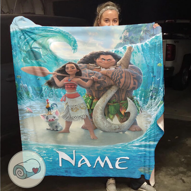 May include: A blue and white blanket featuring characters from the animated movie Moana. The blanket displays Moana, Maui, Pua the pig, and Hei Hei the rooster, with a wave and ocean background. The word "Name" is printed on the blanket.