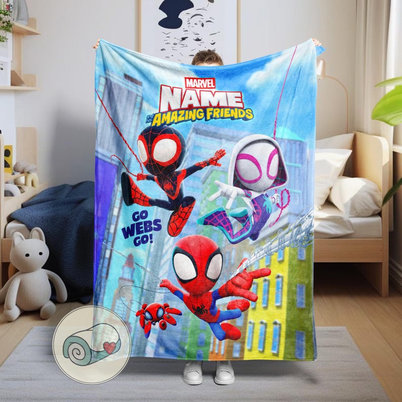 May include: A blue blanket featuring Marvel's Spider-Man and friends. The blanket has a cityscape background and the words "Marvel Name & Amazing Friends" and "Go Webs Go!" printed on it. The blanket is held up by a person.