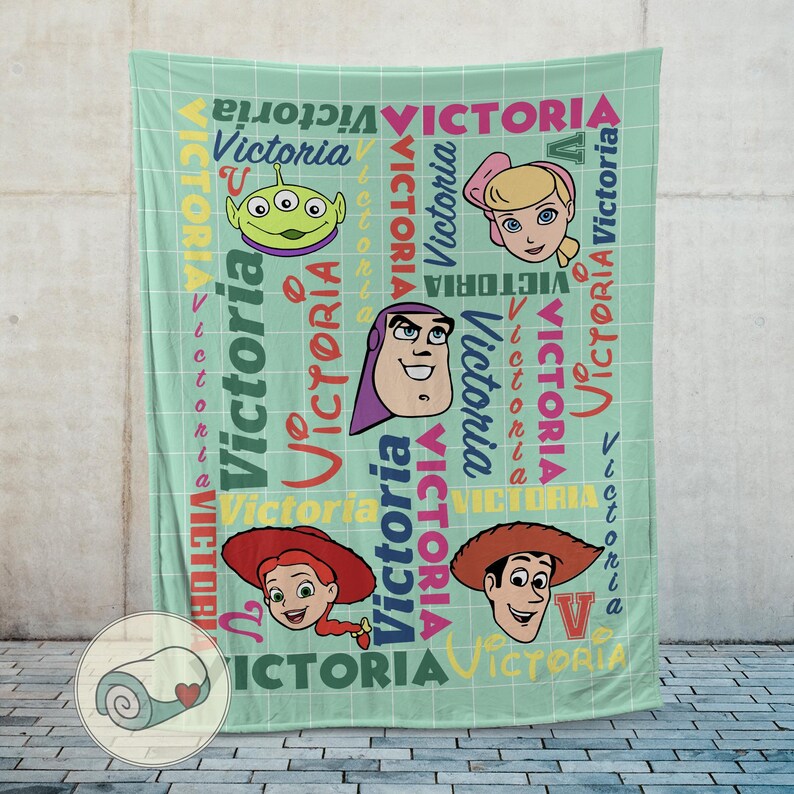 K&ouml;nnte beinhalten: Eine hellgr&uuml;ne Decke mit Gesichtern von Zeichentrickfiguren und dem Namen "Victoria" in verschiedenen Schriftarten. Die Decke hat ein Gittermuster und zeigt Bilder eines gr&uuml;nen Aliens, Buzz Lightyear, Jessie, Bo Peep und Woody.