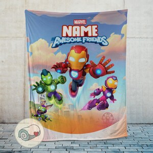 K&ouml;nnte beinhalten: Eine Marvel-Decke mit Iron Man und anderen Charakteren. Die Decke hat einen blauen Himmelshintergrund mit den Worten "MARVEL NAME Awesome Friends" in einem farbenfrohen Design. Die Decke wird vor einer grauen Wand gezeigt.