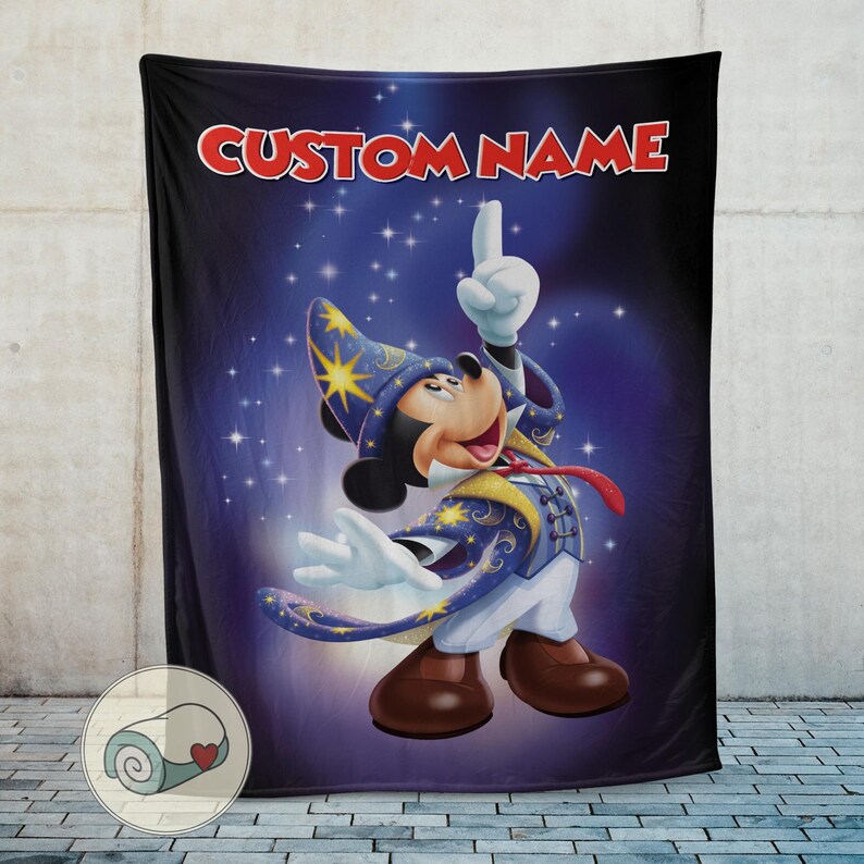 Op de afbeelding: Een zwarte deken met Mickey Mouse in een tovenaarskostuum, met de tekst "CUSTOM NAME" in het rood. Mickey wijst omhoog tegen een sterrenblauwe achtergrond. De deken heeft een opgerold ontwerp in de linkerbenedenhoek.