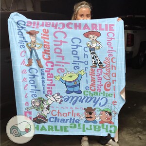 May include: A light blue blanket featuring characters from the Toy Story movie, including Woody, Jessie, Buzz Lightyear, and others. The name "Charlie" is printed repeatedly in various colors across the blanket.