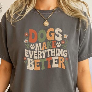 May include: A dark grey t-shirt with the slogan "DOGS MAKE EVERYTHING BETTER" in a retro font with floral and paw print details. The shirt is a Pepper colour.