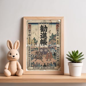 May include: A framed vintage Japanese print with a wooden frame. The print depicts a scene with figures in traditional attire, with Japanese text. A plush bunny and a potted succulent sit nearby on a wooden shelf.