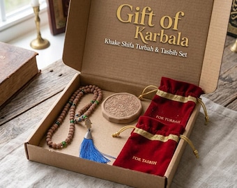 May include: A brown cardboard gift box labelled Gift of Karbala Khake Shifa Turbah & Tasbih Set containing a round clay turbah, a brown beaded tasbih with a blue tassel, and two red velvet drawstring pouches labelled For Turbah and For Tasbih.