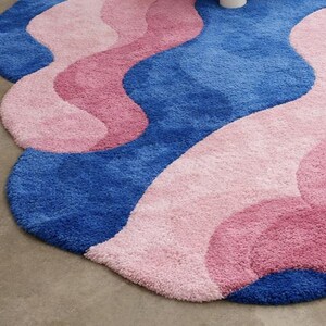 May include: A plush, wavy rug in shades of blue and pink. The rug features a layered design with a soft, textured surface. The color palette includes a deep blue, a medium pink, and a lighter pink, creating a visually appealing pattern.
