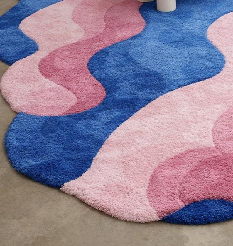 May include: A plush, wavy rug in shades of blue and pink. The rug features a layered design with a soft, textured surface. The color palette includes a deep blue, a medium pink, and a lighter pink, creating a visually appealing pattern.