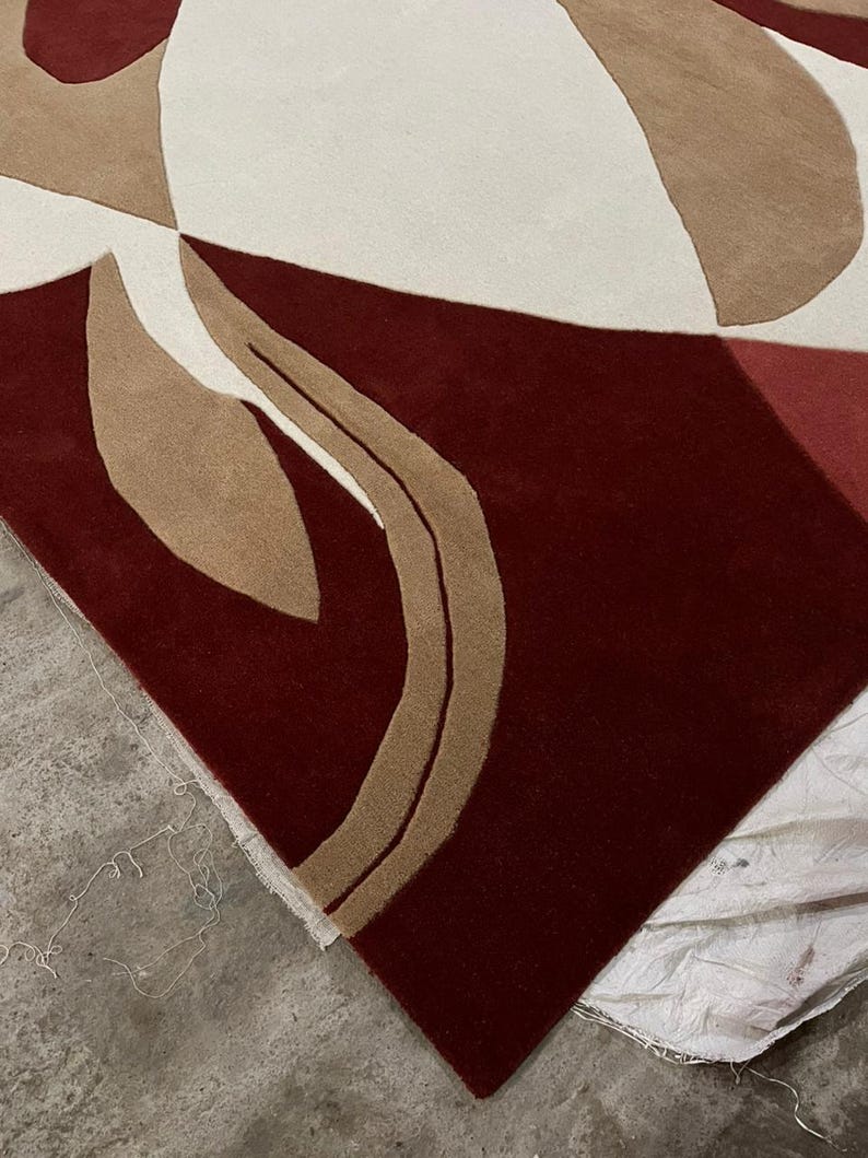 Pu&ograve; includere: Un tappeto moderno con un design astratto. Il tappeto presenta uno sfondo bordeaux scuro con forme geometriche color crema, beige e bordeaux chiaro. Il design del tappeto &egrave; contemporaneo e si adatterebbe a uno spazio abitativo moderno.