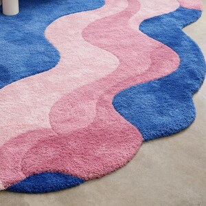 May include: A wavy, plush rug in shades of blue and pink. The rug features a pattern of flowing, organic shapes in varying shades of pink and blue. The rug's design is reminiscent of water or waves.
