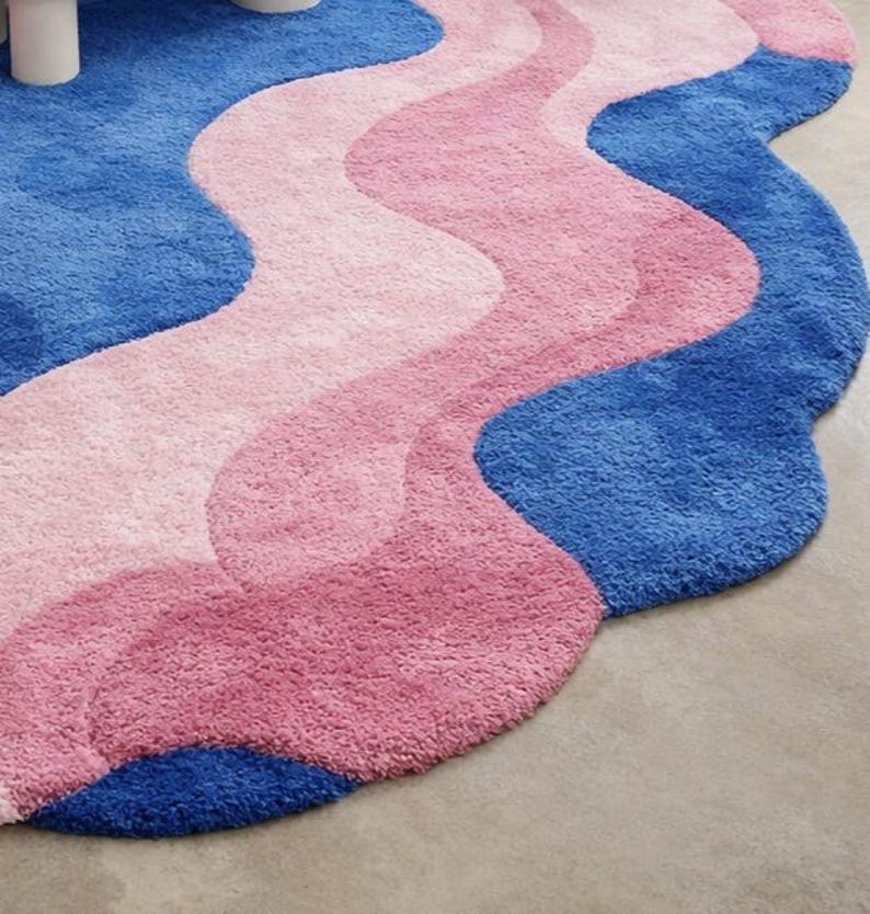 May include: A wavy, plush rug in shades of blue and pink. The rug features a pattern of flowing, organic shapes in varying shades of pink and blue. The rug's design is reminiscent of water or waves.