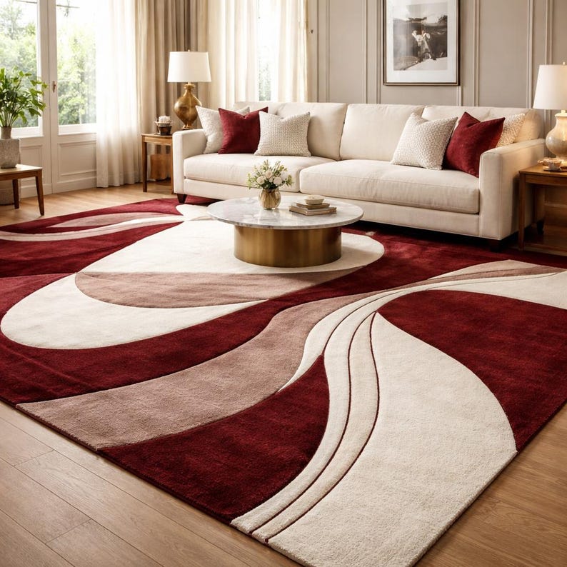 Pu&ograve; includere: Un grande tappeto con un design astratto nei toni del bordeaux, beige e talpa. Il tappeto ha una consistenza morbida e soffice ed &egrave; collocato in un soggiorno con un divano bianco e cuscini. Il design presenta linee e curve fluide.