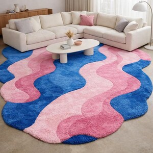 May include: A large, wavy area rug in shades of blue and pink. The rug features a plush, textured surface with a design of flowing, organic shapes. The color palette includes a deep blue, light pink, and a medium pink, creating a vibrant and modern aesthetic.