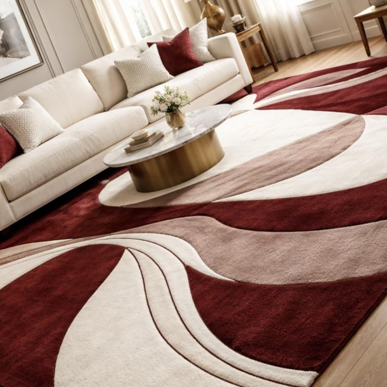 Pu&ograve; includere: Soggiorno con divano color crema e cuscini bordeaux. Un tavolino rotondo con piano in marmo e base dorata poggia su un ampio tappeto. Il tappeto presenta un design a onde bordeaux, crema e talpa, aggiungendo un tocco moderno alla stanza.