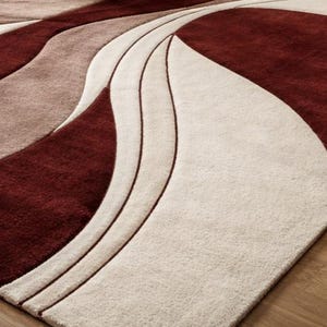 Pu&ograve; includere: Primo piano di un moderno tappeto con un design astratto e fluido. Il tappeto presenta una combinazione di colori, tra cui rosso intenso, beige e marrone chiaro, creando un senso di movimento e profondit&agrave;. La trama del tappeto appare morbida e invitante.