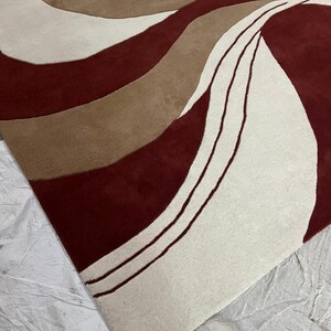 Pu&ograve; includere: Un tappeto moderno con un design astratto. Il tappeto presenta un motivo di linee fluide nei toni del bordeaux, beige e marrone. Il design crea una superficie visivamente dinamica e strutturata. Il design del tappeto aggiunge un tocco contemporaneo a qualsiasi stanza.