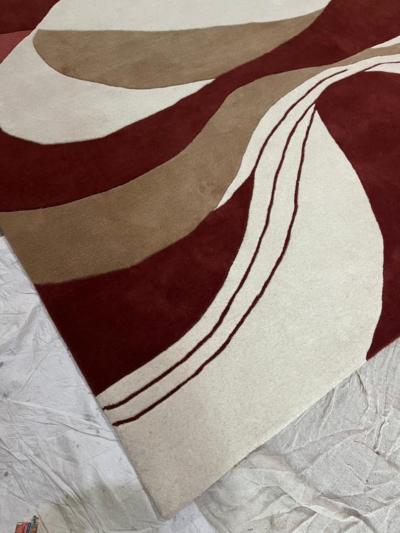 Pu&ograve; includere: Un tappeto moderno con un design astratto. Il tappeto presenta un motivo di linee fluide nei toni del bordeaux, beige e marrone. Il design crea una superficie visivamente dinamica e strutturata. Il design del tappeto aggiunge un tocco contemporaneo a qualsiasi stanza.