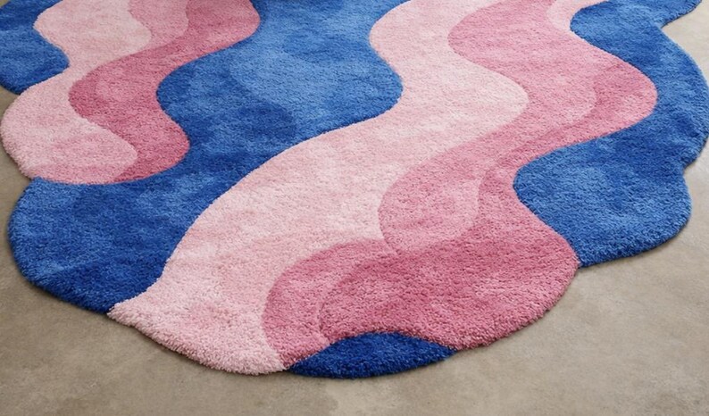 May include: A plush, wavy rug in shades of blue, pink, and rose. The rug has a soft, textured surface and a unique, organic shape. The design features flowing, layered color blocks, adding a modern touch to any space.