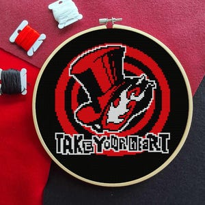 May include: Cross-stitch embroidery in a wooden hoop featuring a red and black design with the text "TAKE YOUR HEART" in white. The design is on a black background with red accents. Spools of red, white, and black thread are visible.
