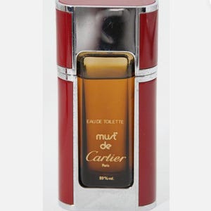 May include: A red and silver bottle of Must de Cartier Eau de Toilette. The bottle is labeled with the words 