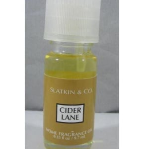 May include: A small clear glass bottle of Slatkin & Co. Cider Lane home fragrance oil with a white ribbed screw cap. The gold label features the text Slatkin & Co. Cider Lane Home Fragrance Oil and the volume measurement of 0.33 fl oz.