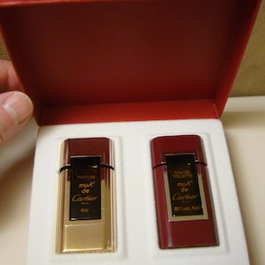 May include: Two miniature perfume bottles in a red box. The bottle on the left is gold with the words 