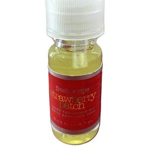 May include: A small glass bottle of home fragrance oil with a white cap. The bottle has a red label with the words "fresh & ripe strawberry patch" in a cursive font. The liquid inside is yellow.