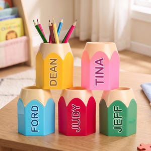 Peut inclure: Cinq porte-stylos hexagonaux en forme de crayon de couleur jaune, rose, bleu, rouge et vert. Chaque porte-stylo porte un nom imprimé en blanc : Dean, Tina, Ford, Judy et Jeff. Le porte-stylo jaune contient plusieurs crayons de couleur empilés.